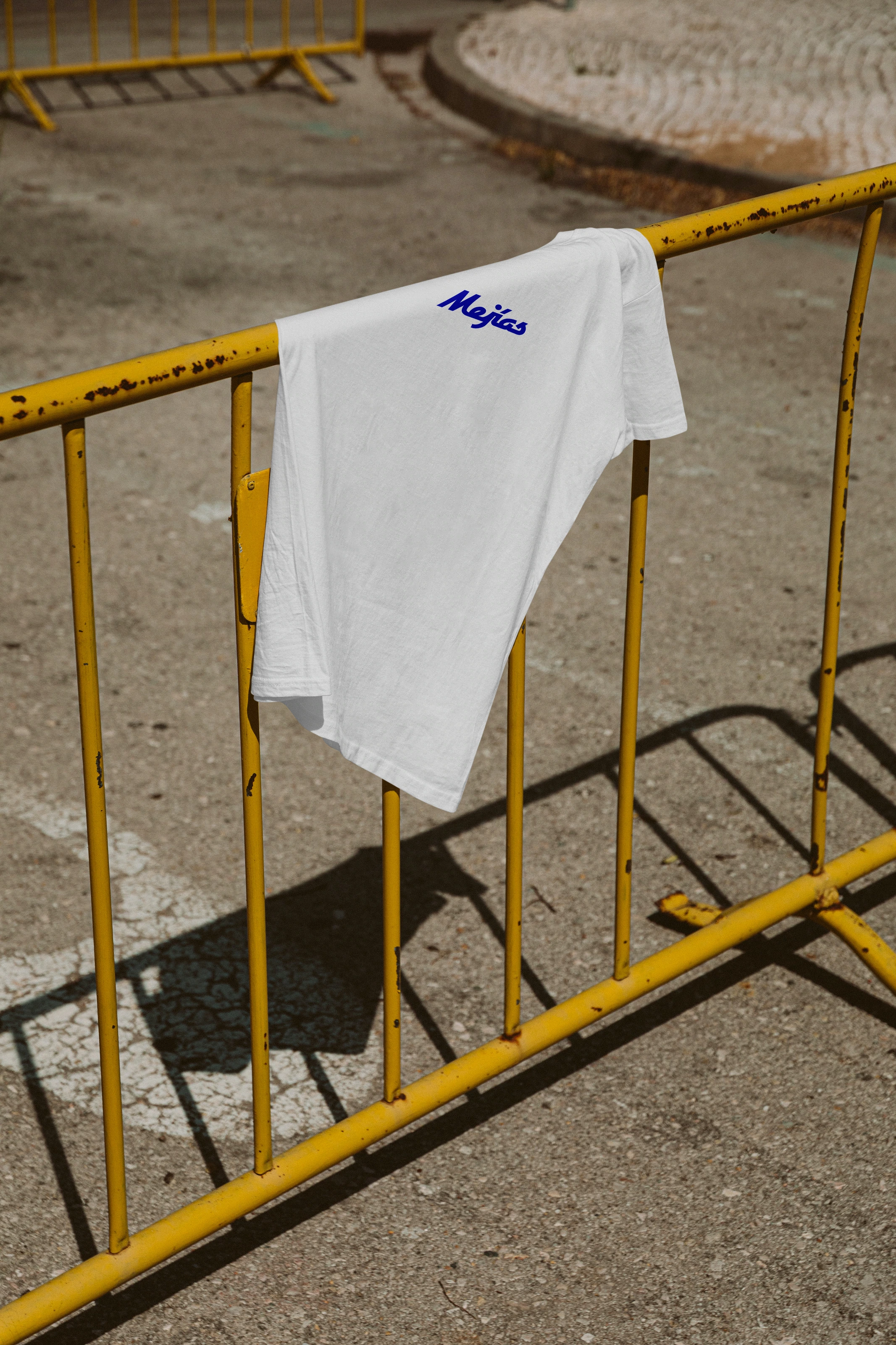 White Mejías T-shirt draped over a yellow street barrier.