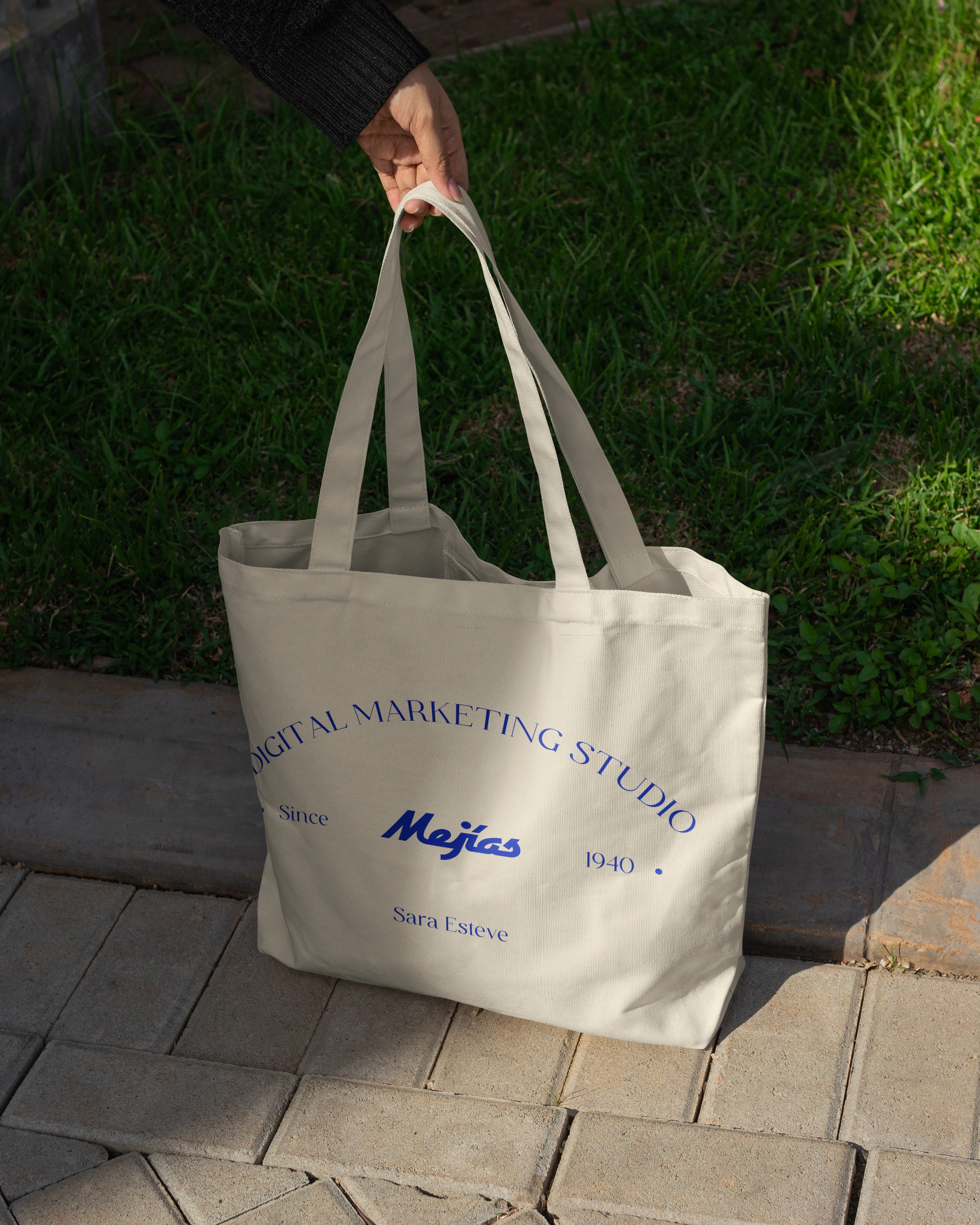 Cream canvas tote bag carrying the Mejías identity in blue, photographed outdoors.